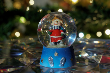 Christmas snow globe ball. Decorating Christmas dome ball before a lit Christmas tree.