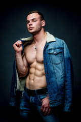 handsome young strong man in jeans jacket posing in studio