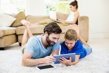 Father and son lying on rug and using digital tablet