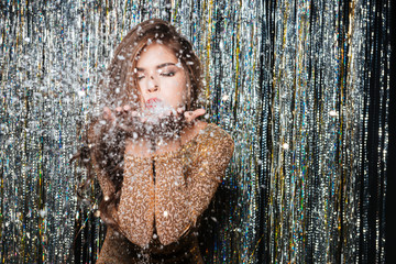 Beautiful woman standing and blowing on snowflakes in her hands