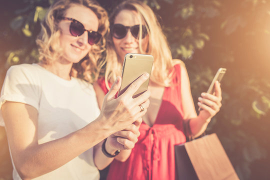 Sunny summer day.Close-up of a smartphone in hands of young women standing outdoors.Focus on smartphone.Girl's faces is blurred.Girl in white t-shirt shows another girl picture on smartphone screen.