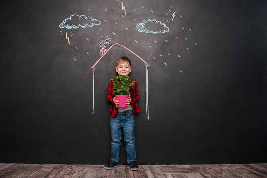 Kid standing in house on chalkboard while holding flower