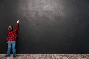 Pretty child standing near blackboard and drawing on it