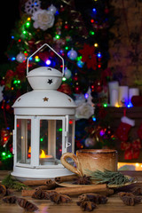 Christmas Decorations with small cup of coffee, lamp with candle, cinnamon sticks, star anise, fir branch on wooden table against lights background