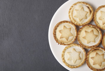A plate full of freshly baked mince pies on a rustic slate background with blank space at side