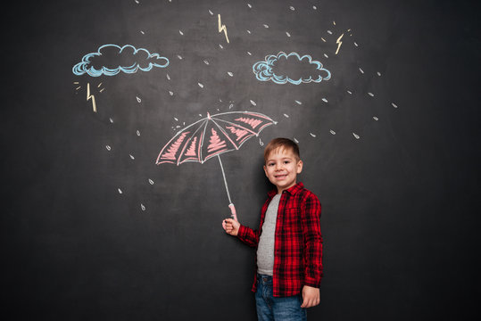Kid looking at camera while holding umbrella on chalkboard