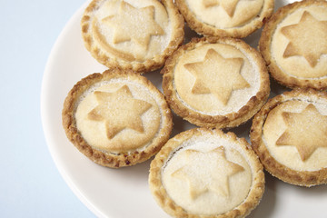 A plate full of freshly baked mince pies on a pastel blue background