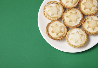 A plate full of freshly baked mince pies on a green background with blank space at side