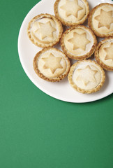 A plate full of freshly baked mince pies on a green background with blank space below