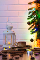 Christmas Decorations with cup of coffee, lamp with candle, cinnamon sticks, star anise, fir branch on wooden table against brick background