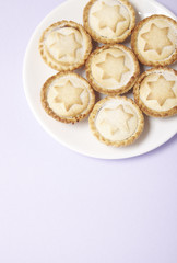 A plate full of freshly baked mince pies on a pastel purple background with blank space below