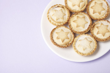A plate full of freshly baked mince pies on a pastel purple background with blank space at side