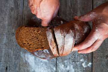 Male hands slicing fresh home-made bread on rustic table