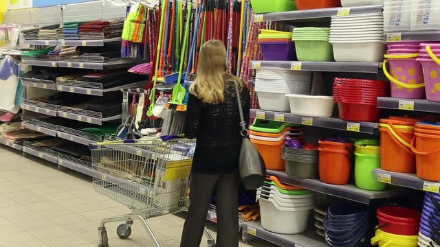 Girl walking with shopping cart in shop, she walks along the row with the goods
