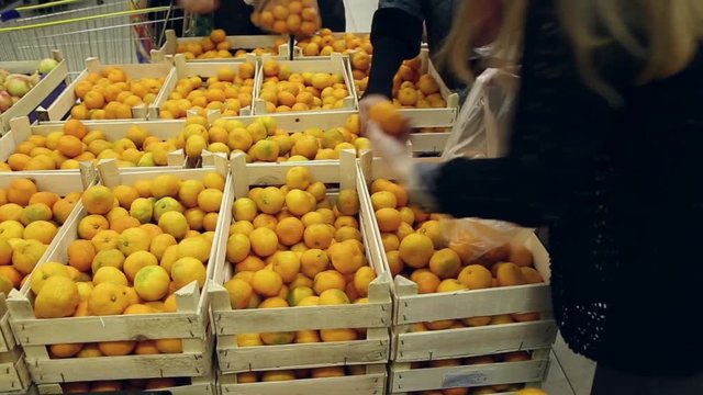 People put tangerines in a bags from the boxes in shop
