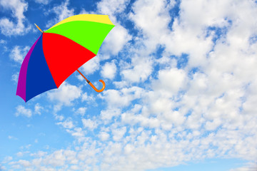 Multicolored umbrella flies in sky against of pure white clouds.Wind of change concept.