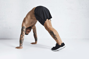 Strong brutal tattoed and ripped male athlete shows how to do pike push-ups, isolated on white...