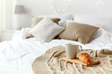 coffee cup and croissant on plaid in bed at home - obrazy, fototapety, plakaty