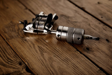 Close focus on shiny steel chrome handmade traditional induction tattoo gun on rustic wooden table