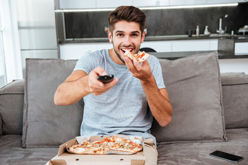 Man holding remote control and pushing button while eating pizza