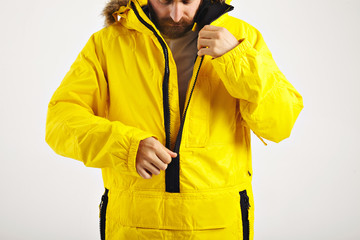 Serious bearded young man zipping up his bright yellow warm snowboarding anorak isolated on white © BublikHaus
