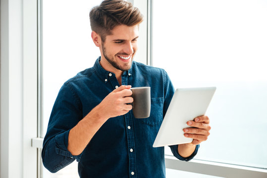 Young happy man holding tablet and drinking coffee