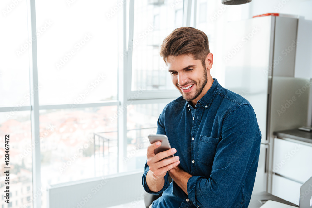 Wall mural young man using a smartphone and smiling indoors