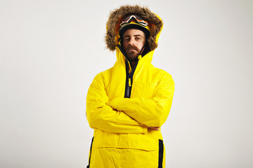 Attractive young man wearing snowboard helmet and goggles and a bright yellow anorak with arms crossed on white background © BublikHaus