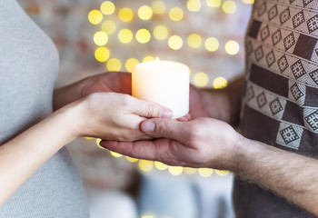 The loving couple holds the burning candle in hand. The woman is pregnant.