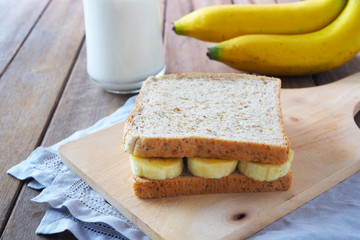Healthy breakfast with banana sandwich, milk and ripe bananas on cutting board.