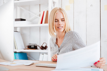 Fototapeta na wymiar Concentrated blonde woman looking through documents while sitting at workplace