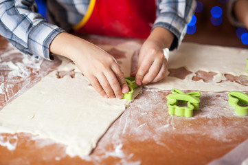 hands of a child who is preparing cookies in the kitchen with flour and dough