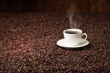 dark roasted offee beans on wooden table with hot coffee cup