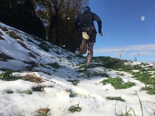 Man running up snow covered grass slope on sunny blue sky day