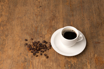 coffee cup with spilled roasted coffee beans on a wooden surface, shot from above