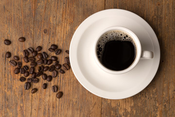 coffee cup on wooden surface with some beans close-up topview