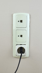 Three old used sockets on a wall - two for network cable and one with black electric plug
