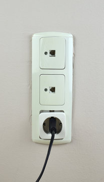 Three old used sockets on a wall - two for network cable and one with black electric plug