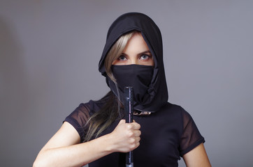 Samurai woman dressed in black with matching veil covering face, holding hand on sword facing camera, ninja concept © Fotos 593