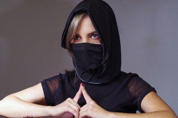 Headshot samurai woman dressed in black with matching veil covering face, resting arms on desk and touching fingertips against each other, facing camera, ninja concept © Fotos 593