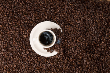 Naklejka premium hot coffee cup on bed of roasted beans, topview