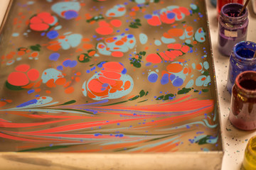 Traditional Turkish art Ebru in process. Woman hand sprinkling paint over water and colourful paint bottles standing next to the ebru tray
