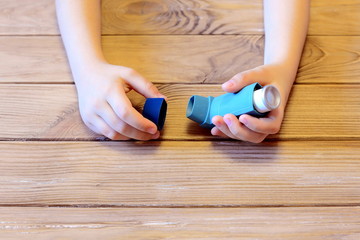 Small child holds asthma inhaler in his hands. Inhalation treatment of respiratory diseases. Allergy and bronchial asthma concept. Old wooden background