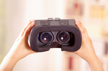 Young brunette woman holding up virtual reality goggles showing to camera, vr concept