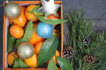 Мандарины и новогодние игрушки в оранжевой коробке и рядом лежит еловая ветка - obrazy, fototapety, plakaty