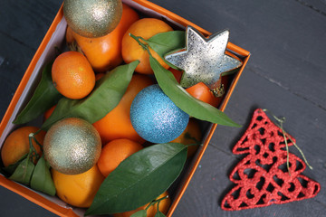 Мандарины и новогодние игрушки в оранжевой коробке и красная елочка на полу - obrazy, fototapety, plakaty