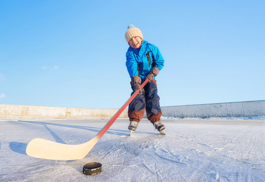 Winter games. Young happy child playing ice hockey on an outdoor ice rink. Focus on the boy.