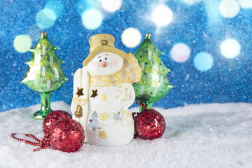 Christmas decoration with snowman figurine, red baubles on a snow shiny blue background.