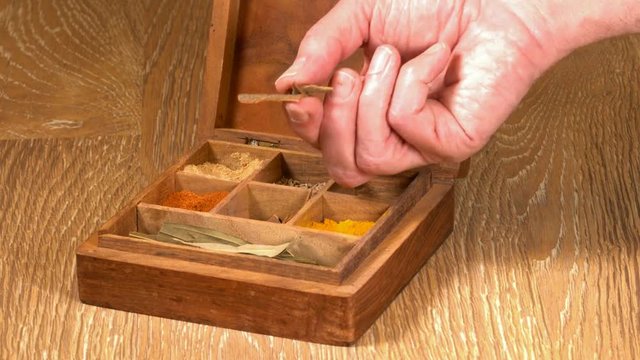 Collection of different oriental indian curry spices in wooden box with cinnamon bark being picked up in senior man hand