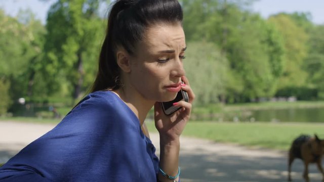 Portrait of unhappy upset young woman talking on mobile phone in sunny park. Human face expression, emotion, bad news reaction.